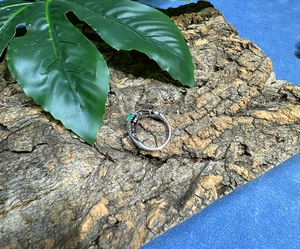 Macro detail of silver ring with heart-cut green gemstone on a natural bark surface