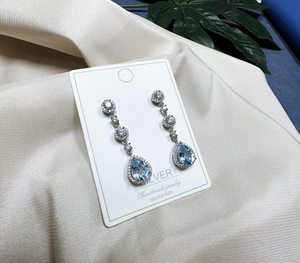 Close-up of pear-cut light blue gemstone earrings in S925 silver on satin background