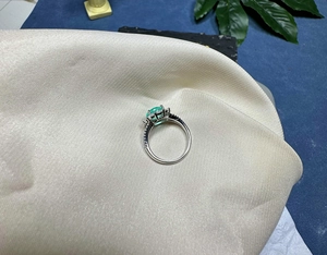 Close-up of an 8mm oval cut green gemstone ring with pavé diamonds on a satin fabric
