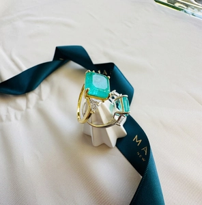 Detailed view of emerald-cut green gemstone ring with gold and silver bands on display
