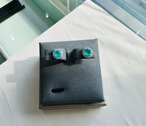 Macro shot of silver stud earrings featuring round emerald center stone and halo diamonds
