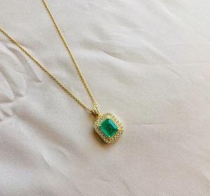 Macro detail of emerald-cut green gemstone pendant with diamond halo on a gold chain