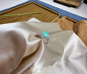Macro detail of 8mm round mint green Paraiba ring with zircon halo on silk fabric