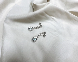 Detailed close-up of pear-cut blue topaz drop earrings on elegant silk fabric background