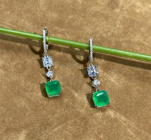 Detail of square emerald cut gemstone earrings hanging on a green plant stem