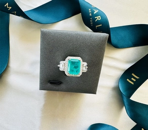 Detail of emerald-cut green gemstone ring with halo diamonds on white satin silk
