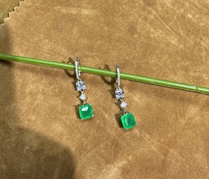 Detail of S925 silver emerald earrings featuring square cut green gems on a green branch