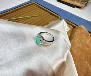 Macro view of oval green gemstone ring with pavé diamond halo and silver band detail