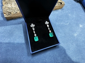 Detail of emerald cut green drop earrings with floral stud in a blue jewelry box