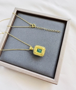 Detail of emerald cut green gemstone pendant with textured gold plated sunburst bezel