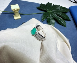 Gros plan d'une bague avec gemme verte marquise et pierres pavées sur tissu satin