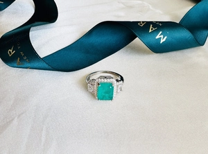 Macro view of emerald cut green gemstone ring with side stones on silk fabric