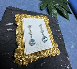 Detail of silver drop earring with pear-cut blue gemstone and round zircon pavé