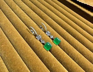 Macro view of square emerald-cut green gemstones on silver drop earrings with zircons