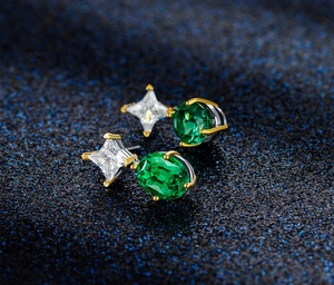 Macro shot of silver star studs with oval emerald green stones and golden prong details