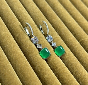 Macro shot of S925 sterling silver emerald earrings with square gemstones on yellow velvet