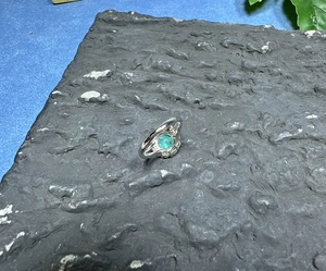 Macro shot of 8mm green gemstone ring with side stones on dark textured stone