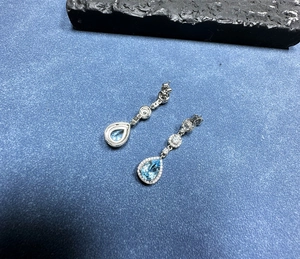 Detailed view of pear-shaped blue topaz earrings in silver setting with white gemstones