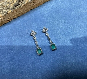 Macro shot of silver drop earrings with emerald-cut green stones on a blue background