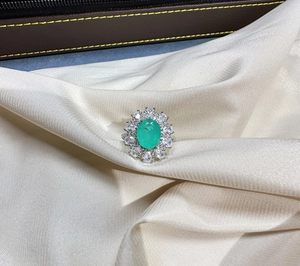 Detailed view of an oval emerald-green gemstone ring on elegant white silk background