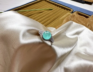 Macro shot of 8mm round blue-green gemstone ring with pavé stones on silk