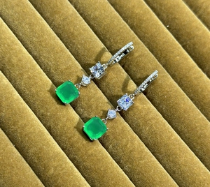 Close-up of S925 silver drop earrings with square emerald gemstones on a velvet tray