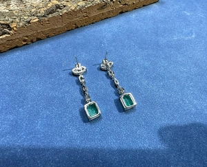 Detailed macro view of silver earrings featuring rectangular emerald-green gemstones