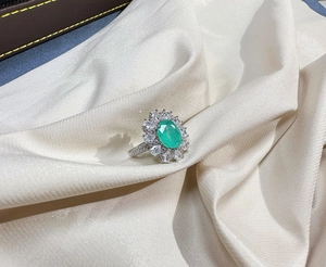 Detailed close-up of oval green Paraiba gemstone ring with diamonds on white silk fabric