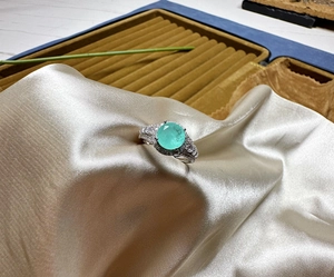 Close-up of mint green Paraiba gemstone ring with pavé diamonds on champagne satin fabric