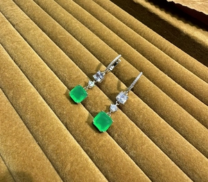 Macro view of square emerald-cut green gemstones on silver drop earrings with zircons