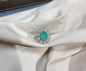 Macro detail of oval Paraiba gem ring on cream silk with halo cluster diamond setting