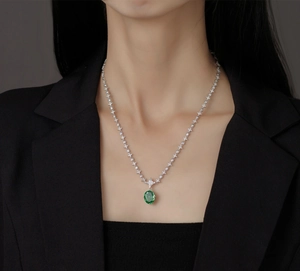 Close-up of a silver necklace featuring a large oval green emerald gemstone on a model