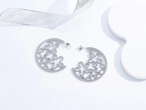 Macro detail of silver C-hoop earrings featuring hollow flower patterns and micro-pavé zircons