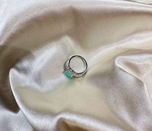 Detail of silver ring with 8mm oval green gemstone and pavé-set diamonds on silk