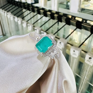 Classic 8x10mm emerald-cut green gemstone ring with halo diamonds on satin fabric