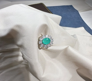 Detailed close-up of oval green gemstone ring with double halo stones on satin