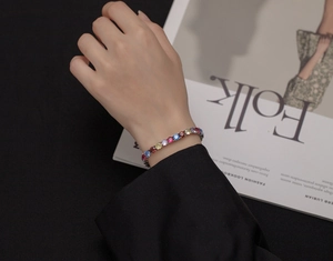 Dettaglio macro del bracciale tennis arcobaleno con pietre colorate sul polso di una donna