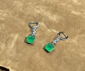 Macro view of square emerald-cut green gemstone earrings in silver setting with zircon stones