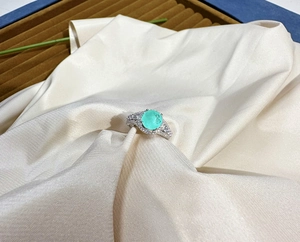Macro shot of silver ring with mint green gemstone and pavé-set zircons on satin