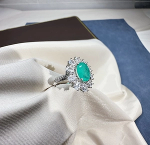 Macro detail of oval green gemstone ring with sparkling diamond halo on silk