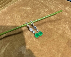 Macro detail of emerald-cut green gemstone earrings with silver dangling hooks