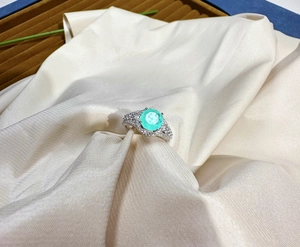 Detailed close-up of 8mm Paraiba gemstone ring with pavé diamonds on cream satin