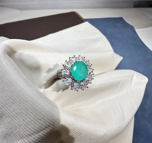 Macro detail of oval green gemstone ring with pear-cut halo on white silk fabric