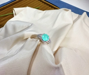 Detailed macro view of 8mm round Paraiba gemstone ring with pavé stones on a silk fabric