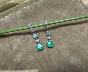 Macro shot of 925 silver emerald drop earrings hanging on a green natural stem branch