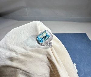 Macro shot of 8x12mm aquamarine ring with diamond halo on soft silk fabric