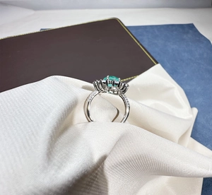 Detail of an oval green gemstone ring with micro-paved diamonds on white satin