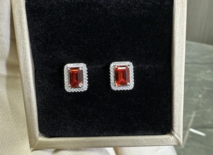Macro view of 925 silver stud earrings with emerald-cut red ruby and zircon halo