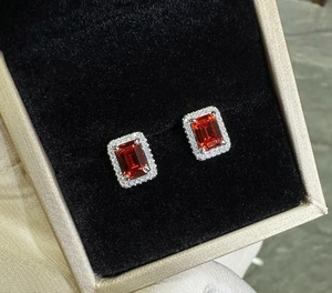 Macro view of emerald-cut ruby earrings with zircon halo in a velvet jewelry box