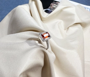 Macro shot of 925 silver halo ring with emerald-cut orange gemstone on satin fabric